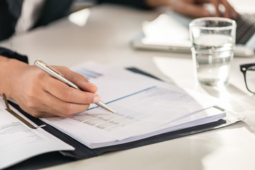 Close-up of the hands of a business woman sitting at desk while checking numbers printed on paper