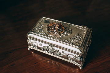 Golden rings of the newlyweds on an old silver box.