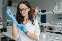 Woman Putting On Gloves In Lab