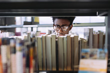 Man Searching Books In Shelf At Library