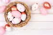 Springtime nest with rose gold, pink and white painted Easter Eggs against a rustic white wood background