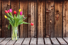 Bunch Of Colorful Tulips In A Clear Vase On A Rustic Plank Table.