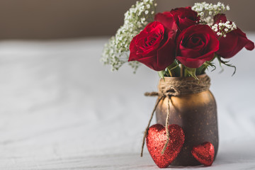 close up view of a vase with roses and two hearts in front of it with dead space on the left