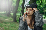Fototapeta  - Młoda kobieta rozmawia przez telefon w parku.