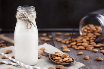 Organic white almond milk in a glass bottle with whole almonds spilled over a rustic wooden table.