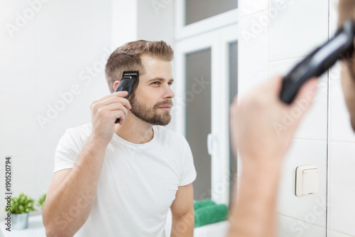 Fotomural Handsome man cutting his own hair with a clipper