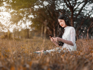 Sticker - woman with headphones listening to music from smart phone and sitting in park