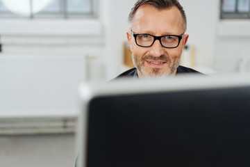 Wall Mural - Businessman smiling over his desktop monitor