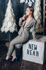 Beautiful girl in a gray suit sits on a cube in a Christmas decor