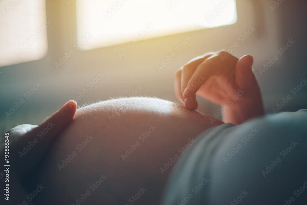 Pregnant woman cuddling belly in bedroom at home