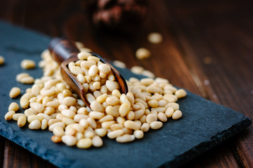 Poster - Natural organic pine nuts on a black slate with scoop.