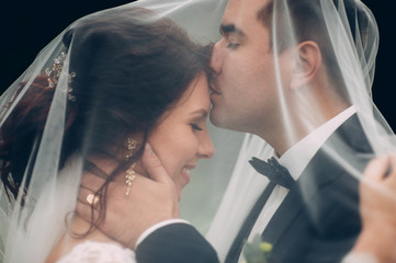 Just married couple kiss standing under a veil in the shine of m