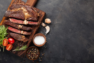 Grilled ribeye beef steak with red wine, herbs and spices on a dark stone background. Top view with copy space for your text