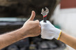 Mechanic hand checking and fixing a broken car in garage.hand of mechanic with thumbs up and tool