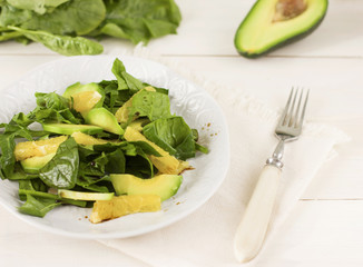 Raw salad of spinach, avocado and orange on a white wooden background