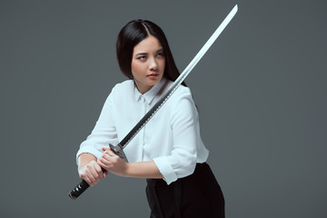 Wall Mural - beautiful asian girl holding katana sword and looking away isolated on grey