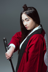 Wall Mural - young asian woman in kimono holding katana and looking at camera isolated on grey