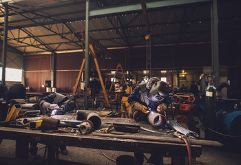 Welder in protective uniform and mask welding metal pipe on the industrial table while sparks flying.