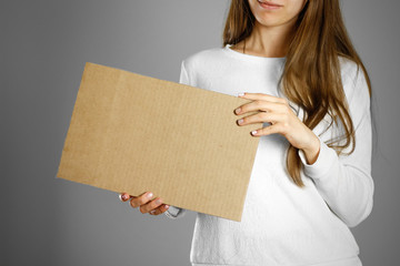 Wall Mural - A young girl in a white jacket holding a piece of cardboard. Prepared for your text