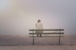 Anonyme junge Frau sitzt betrübt und einsam auf einer Bank im Nebel