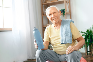 Wall Mural - Senior man exercise at home sitting on exercise ball rest drinking water