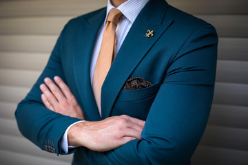 Wall Mural - Man in custom tailored suit with athletic build posing with his hand crossed in front of background