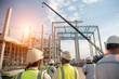 © bannafarsai - Construction engineers supervising progress of construction project stand on new concrete floor top roof and crane background