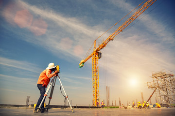 Surveyor builder Engineer with theodolite transit equipment at construction site outdoors during surveying work