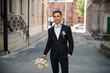 © fesenko - groom in a black suit walking down the street holding a pink bouquet