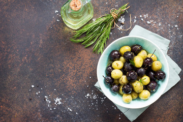 Wall Mural - Culinary background. Olives, green olives with olive oil, fresh rosemary and spices on a stone or slate background. Top view with a copy.