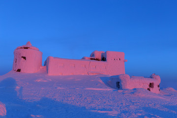 Breathtaking sunrise scenery in mountains. Winter snowy landscape. Scene with snow capped old Polish desolate observatory called White Elephant on summit of mountain Pip Pop Ivan in Chenrnogora ridge.