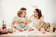 Mother, father and daughters are painting eggs. Happy family are preparing for Easter. 