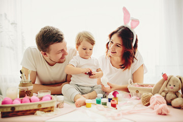 Mother, father and daughters are painting eggs. Happy family are preparing for Easter. 