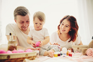 Mother, father and daughters are painting eggs. Happy family are preparing for Easter. 