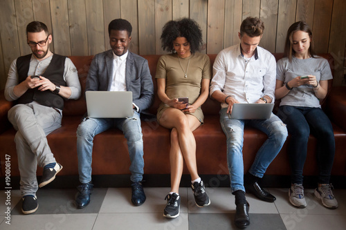 Fotografía Multicultural young people using laptops and smartphones sitting in row, diverse