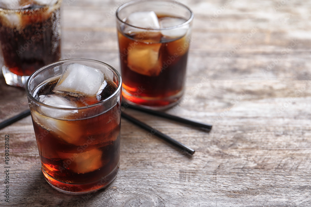 Glasses of refreshing cola with ice on wooden table