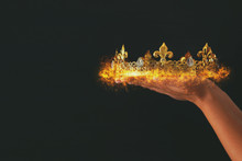 Woman's Hand Holding A Burning Crown Over Black Background.