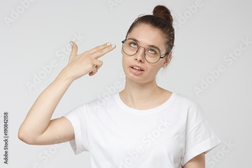 Fotografie, Obraz Young woman committing suicide with finger gun gesture, shooting herself making