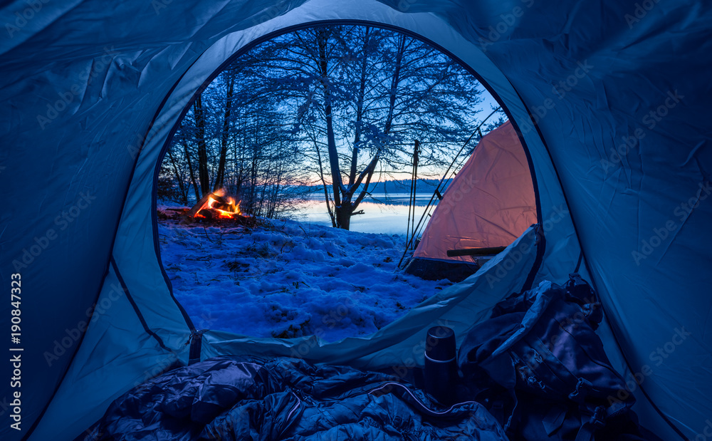 Camp by the lake with campfire at dusk in winter - obrazy, fototapety, plakaty 