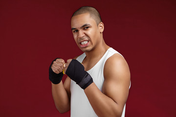 People, sports, boxing and martial arts concept. Portrait of angry muscular young dark skinned kickboxer in white tank top gritting teeth and clenching fists, ready to beat his enemy in the ring