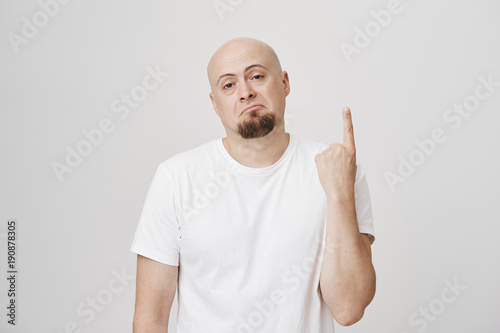 Portrait Of Gloomy And Unsatisfied Bald European Man With Beard Showing Index Finger Or Number One Expressing Disappointment And Looking Gloomy At Camera Over Gray Background Buy This Stock Photo And adobe stock