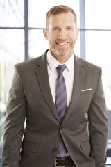 Wall Mural - Successful businessman portrait. Middle aged financial director businessman sitting at office and looking at camera. Wearing elegant suit with tie.