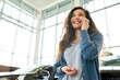 © Seventyfour - Low angle view of attractive mixed race woman looking away with charming smile and talking to her friend on smartphone while choosing new car in showroom, portrait shot