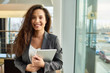 © Seventyfour - Waist-up portrait of attractive young businesswoman in formalwear posing for photography with charming smile while holding digital tablet in hands, interior of spacious office lobby on background