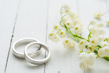 Lily of the valley with wedding rings on white wooden