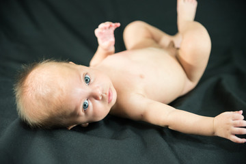 blue eyed naked baby lying on black fabric