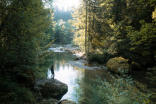 Calm Forest With River And Female Hiker Standing On A Stone Overlooking The Water In Germany