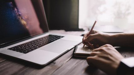 Fototapete - Man is writing on draft notepad and using laptop computer at home office. Freelance lifestyle workplace