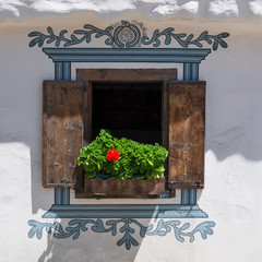 Window on a white wall. Vintage.  Decoratively painted window on the wall of the house. Flower on the windowsill. Wooden shutters. Vintage houses in the canton of Graubunden.