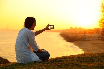 Poster - Woman taking photos with a smart phone at sunset